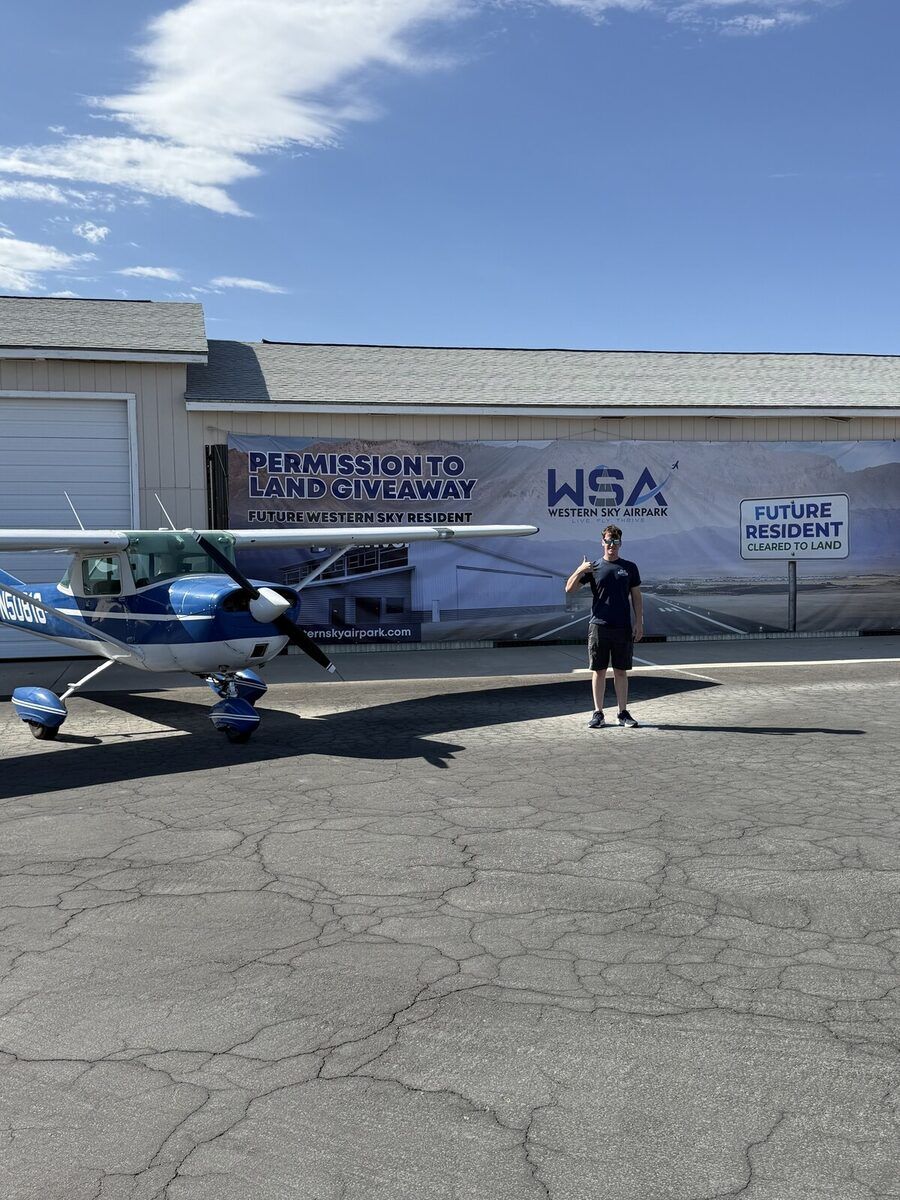 Hayden Bradley with his Cessna in front of the Permission to Land banner at Western Sky Airpark